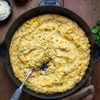 Skillet of Butternut Squash Risotto with a spoon in it on a wooden table from overhead.