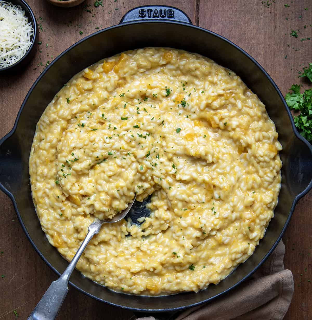 Skillet of Butternut Squash Risotto with a spoon in it on a wooden table from overhead.