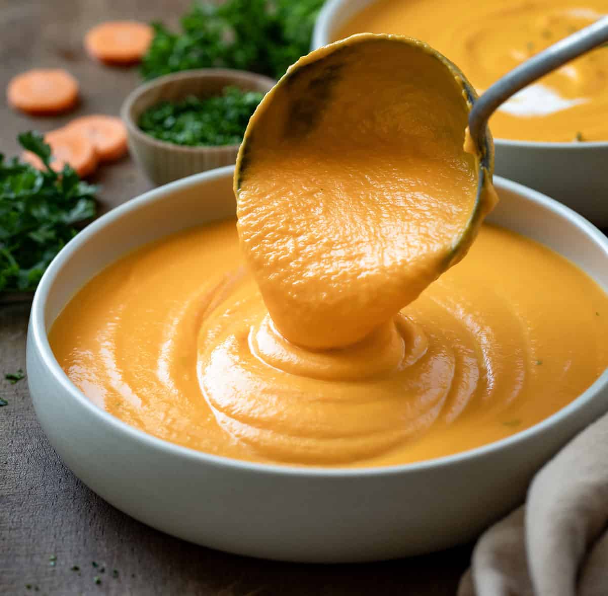 Using a soup ladle to add carrot soup to a bowl.