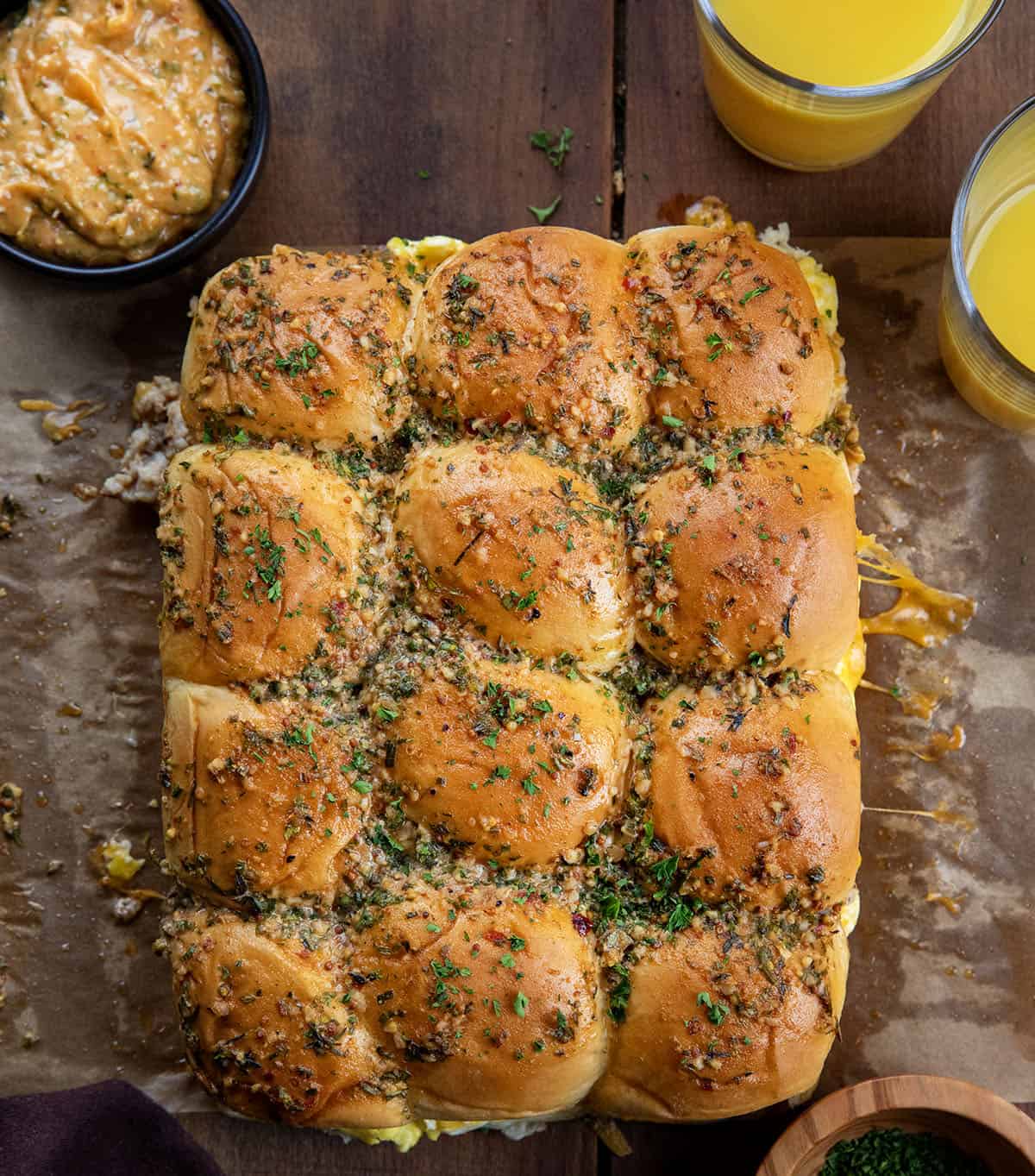 Looking down at Cowboy Breakfast Sliders on a wooden table with orange juice and cowboy butter.