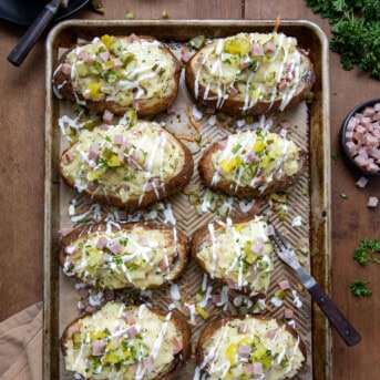 Sheet pan of Dill Pickle and Ham Twice Baked Potatoes with one cut in half and a fork on the sheet pan.