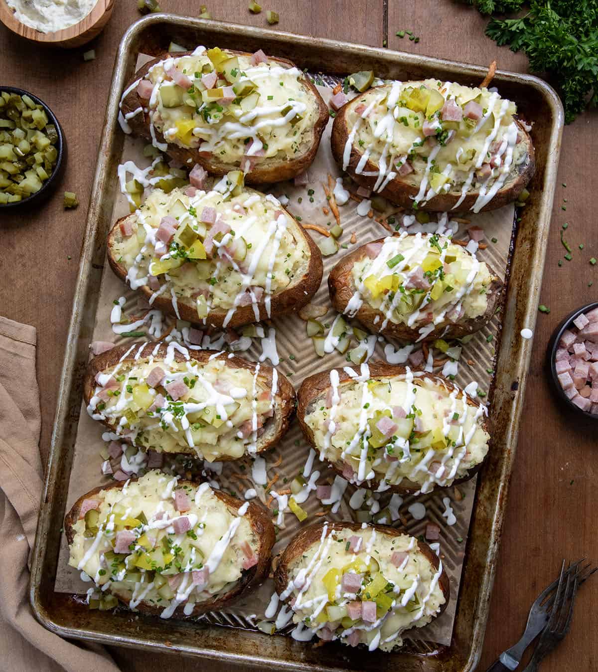 Dill Pickle and Ham Twice Baked Potatoes on a sheet pan with fresh diced ham and fresh diced pickle on a wooden table from overhead.