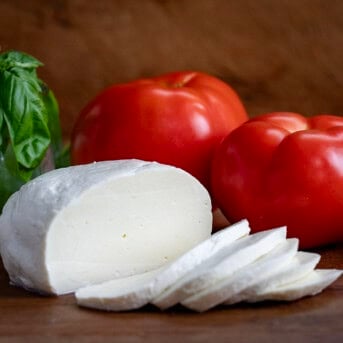 Fresh Homemade Mozzarella sliced on a cutting board with tomatoes and basil.