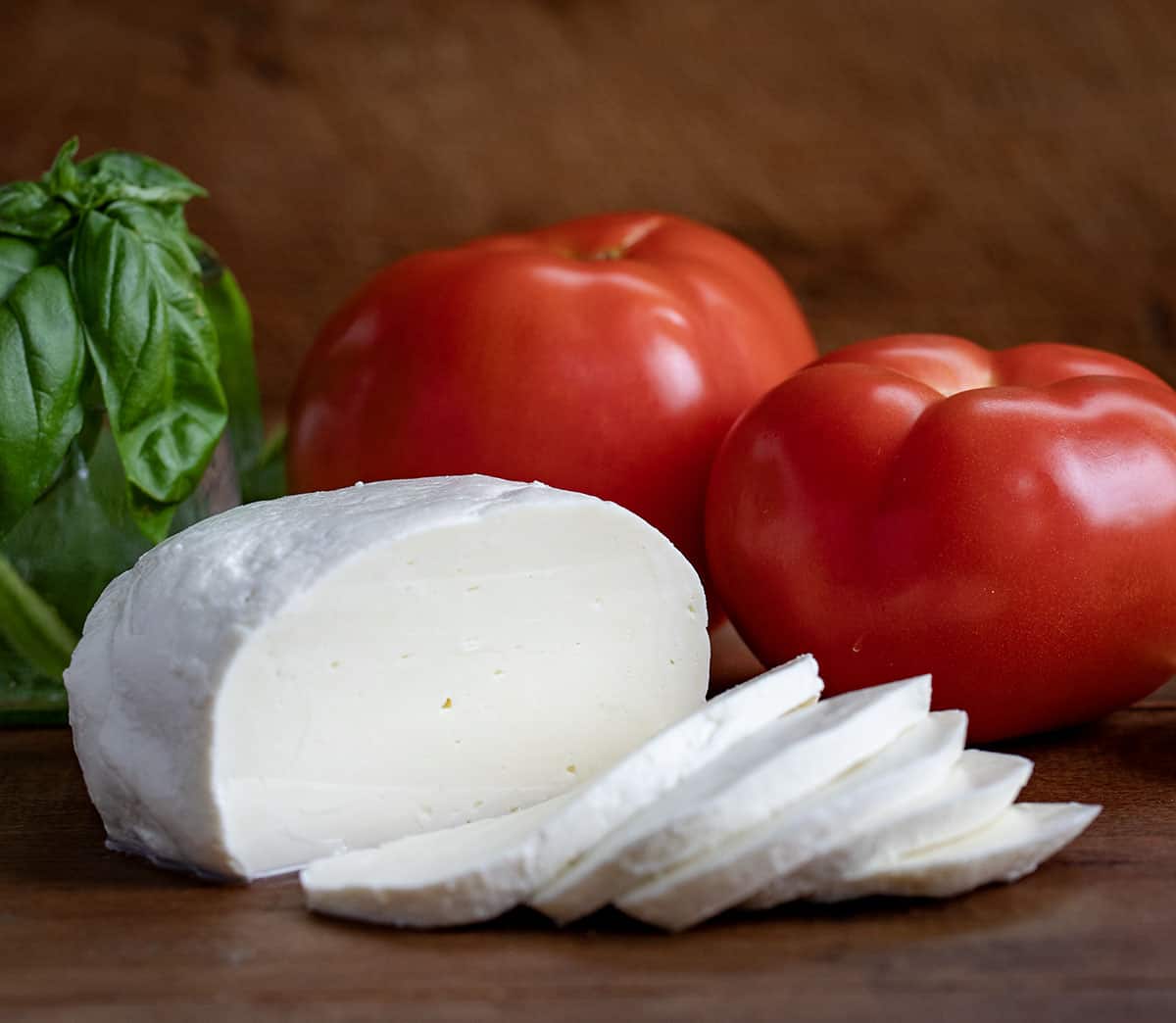 Fresh Homemade Mozzarella sliced on a cutting board with tomatoes and basil.