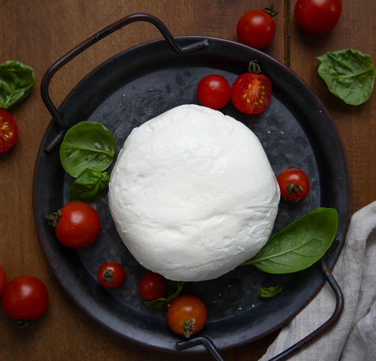 Tray of Homemade Mozzarella on a wooden table with tomatoes and basil from overhead.