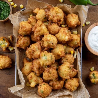 Pan of Jalapeno Corn Nuggets on a wooden table with fresh corn and jalapeno and dipping sauce shot from overhead.