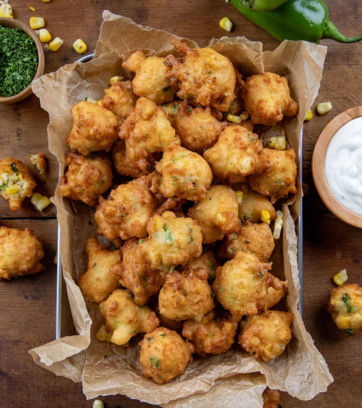 Pan of Jalapeno Corn Nuggets on a wooden table with fresh corn and jalapeno and dipping sauce shot from overhead.