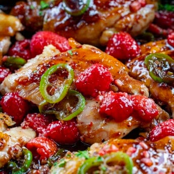 Close up of a Skillet of Jalapeno Raspberry Chicken covered in fresh raspberries and jalapeno.