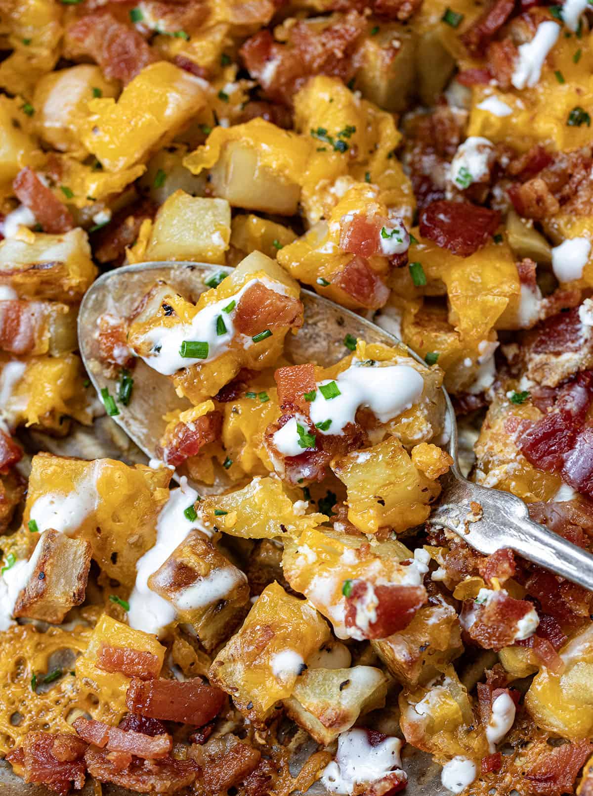 Close up of Loaded Roasted Potatoes with a spoon in the pan.