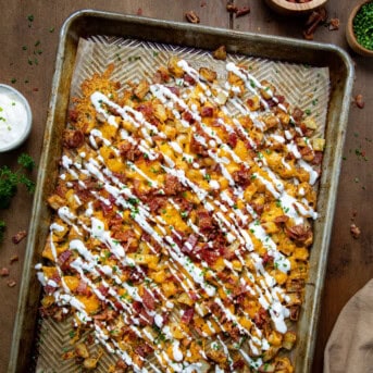 Sheet pan of Loaded Roasted Potatoes on a wooden table from overhead.