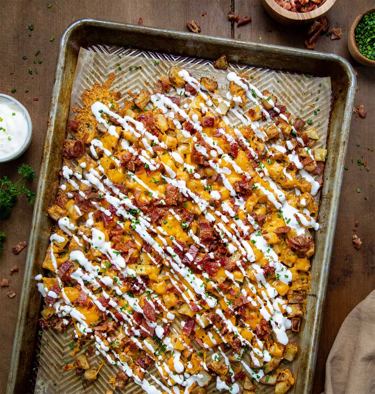 Sheet pan of Loaded Roasted Potatoes on a wooden table from overhead.