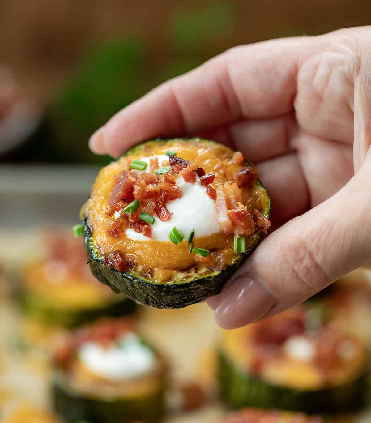 Hand holding a Loaded Zucchini Bite above the tray.