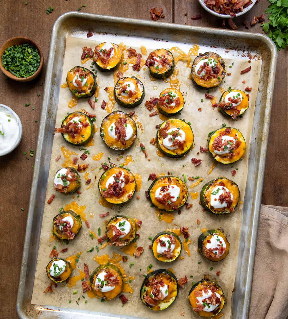 Sheet pan full of Loaded Zucchini Bites on a wooden table from overhead.