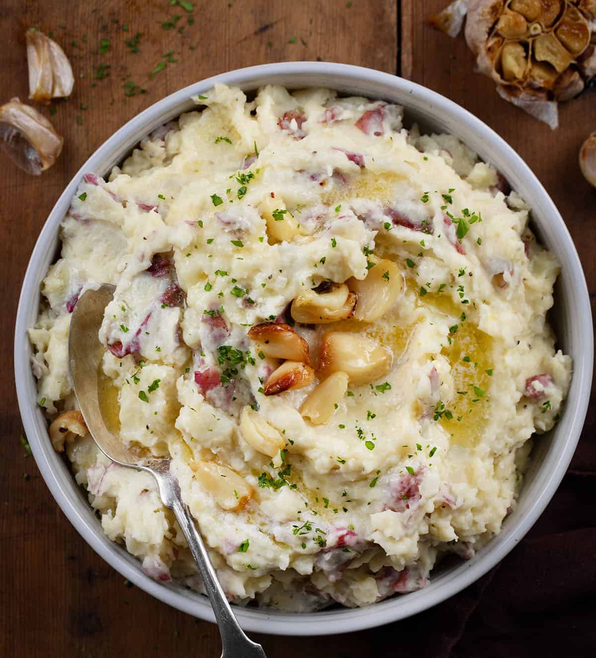 Bowl of Roasted Garlic Mashed Potatoes on a wooden table with a spoon in it.