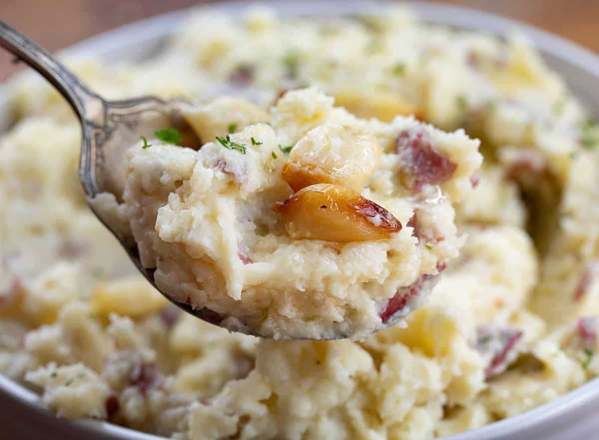 Spoonful of mashed potatoes with a piece of roasted garlic on it.