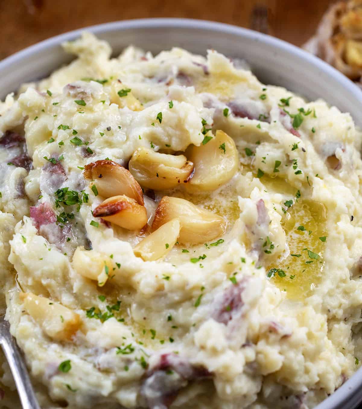 Close up of a bowl of Roasted Garlic Mashed Potatoes with whole roasted garlic on it.