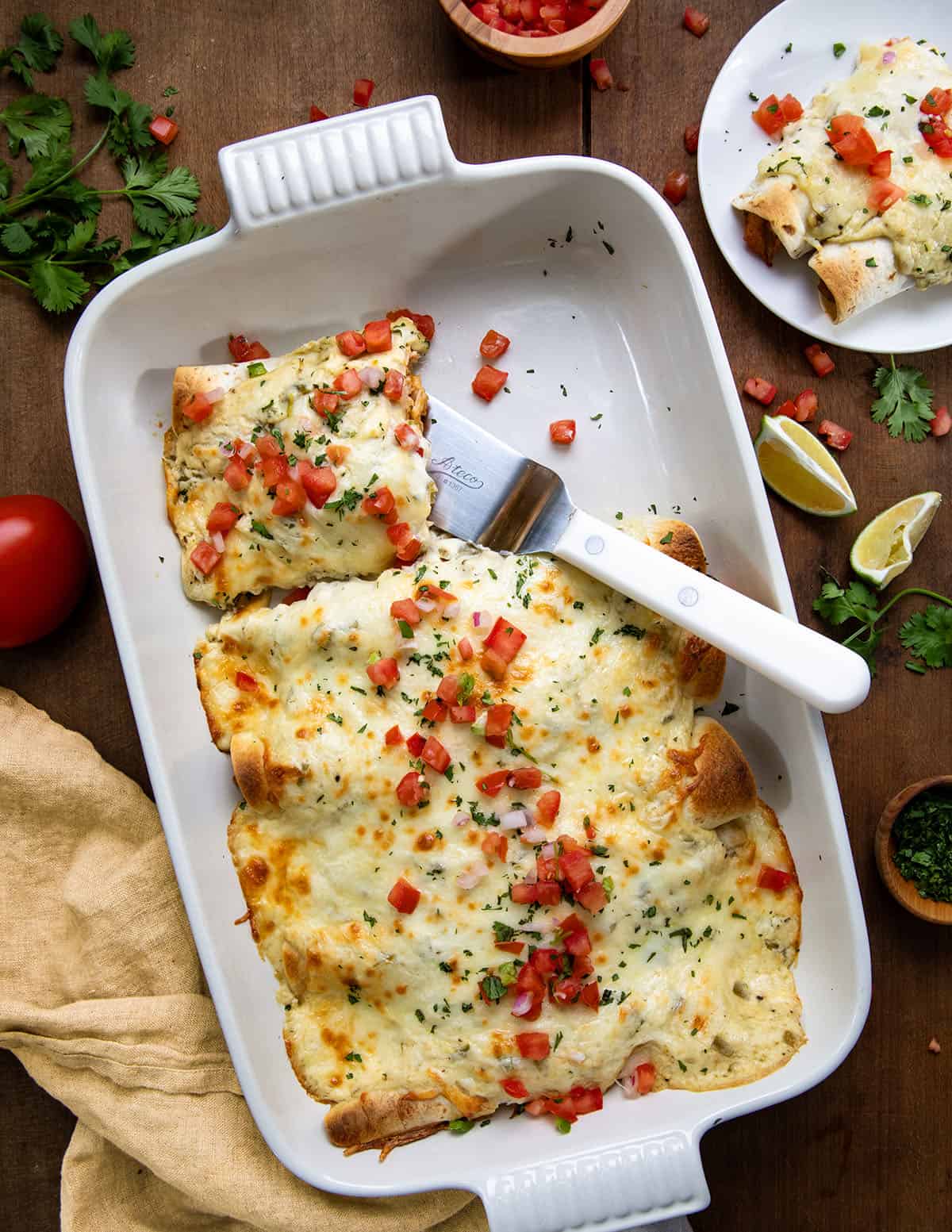 Pan of White Chicken Enchiladas on a wooden table with half an enchilada removed.