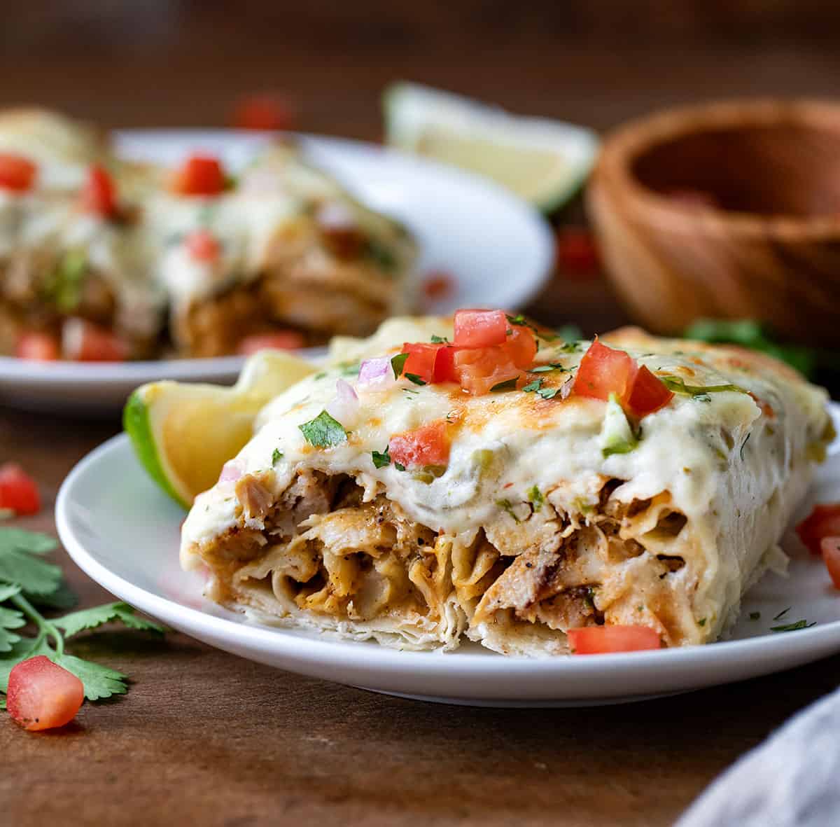 Halved White Chicken Enchiladas on a white plate on a wooden table close up.