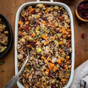 Serving plan of Wild Rice Stuffing with a spoon in it on a wooden table from overhead.