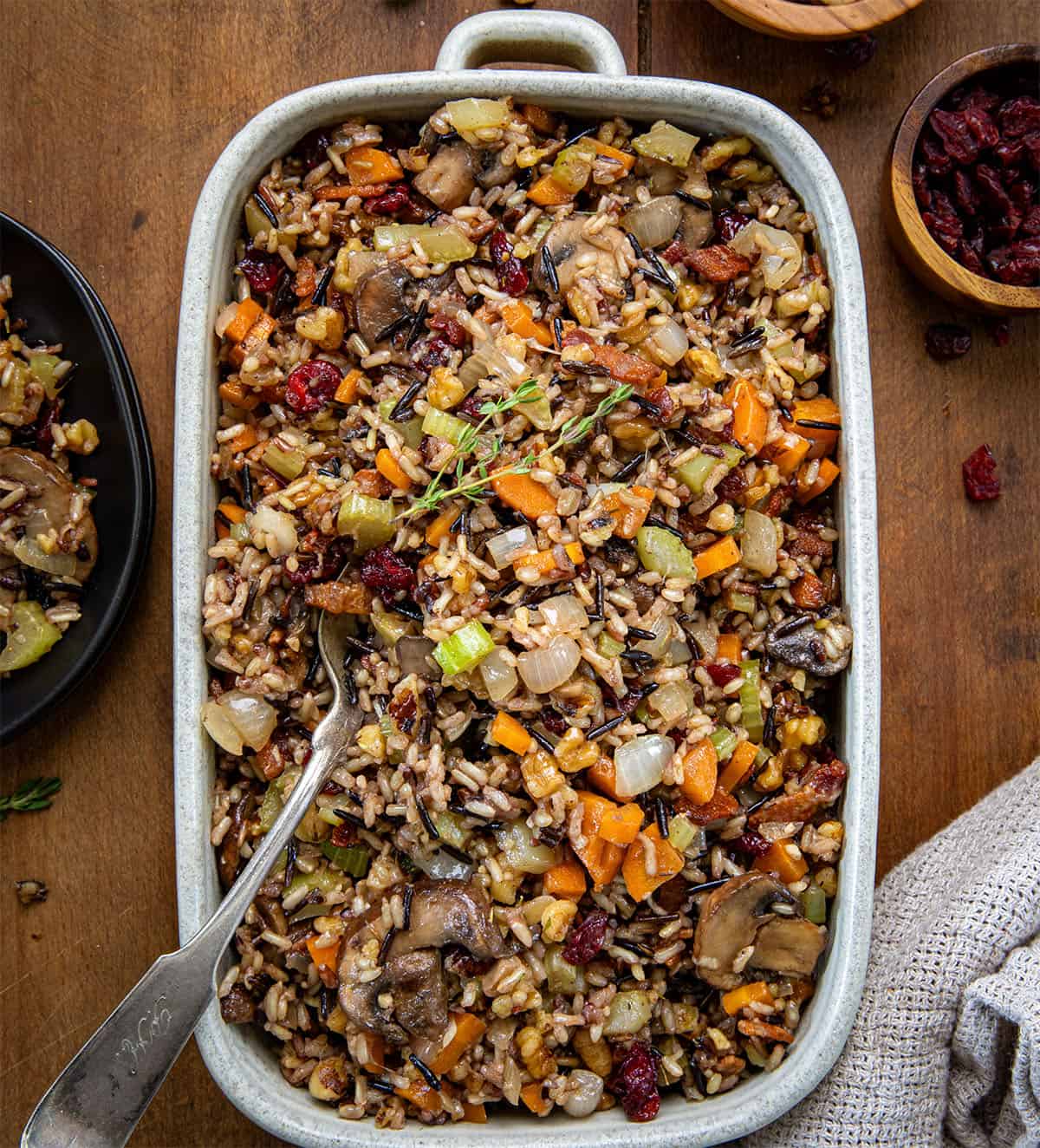 Serving plan of Wild Rice Stuffing with a spoon in it on a wooden table from overhead.