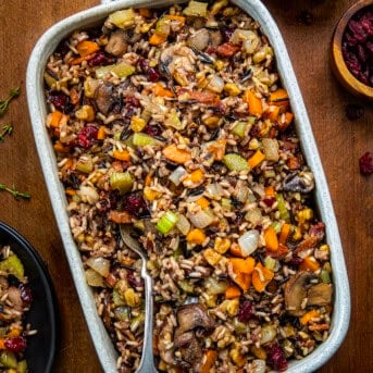 Serving plan of Wild Rice Stuffing with a spoon in it on a wooden table from overhead.