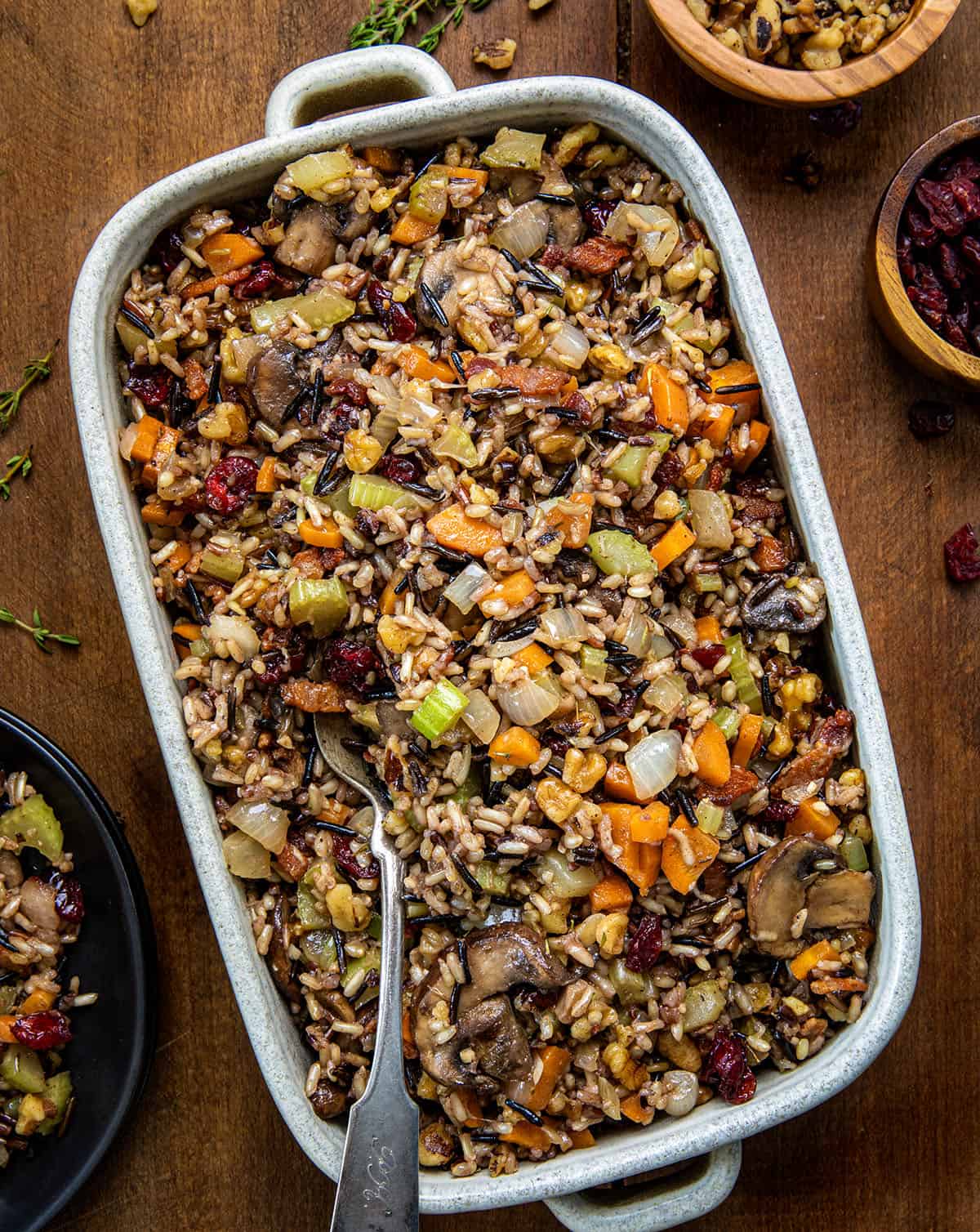 Serving plan of Wild Rice Stuffing with a spoon in it on a wooden table from overhead.