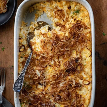 French Onion Funeral Potatoes in a pan with some removed and spoon left in pan on a wooden table.