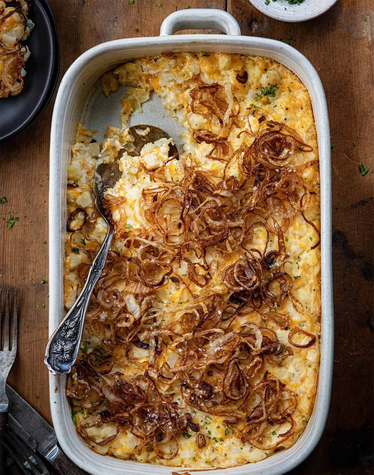 French Onion Funeral Potatoes in a pan with some removed and spoon left in pan on a wooden table.