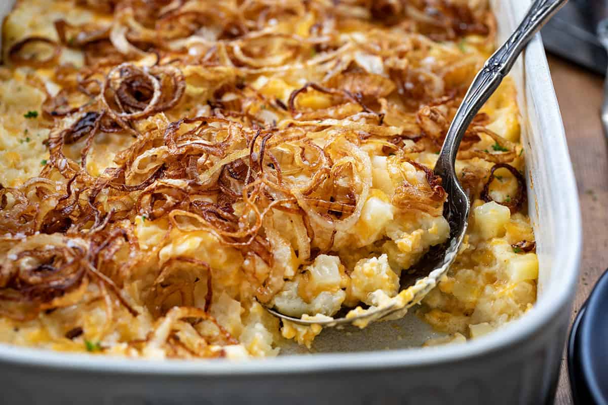 Spoon scooping out some French Onion Funeral Potatoes from pan.