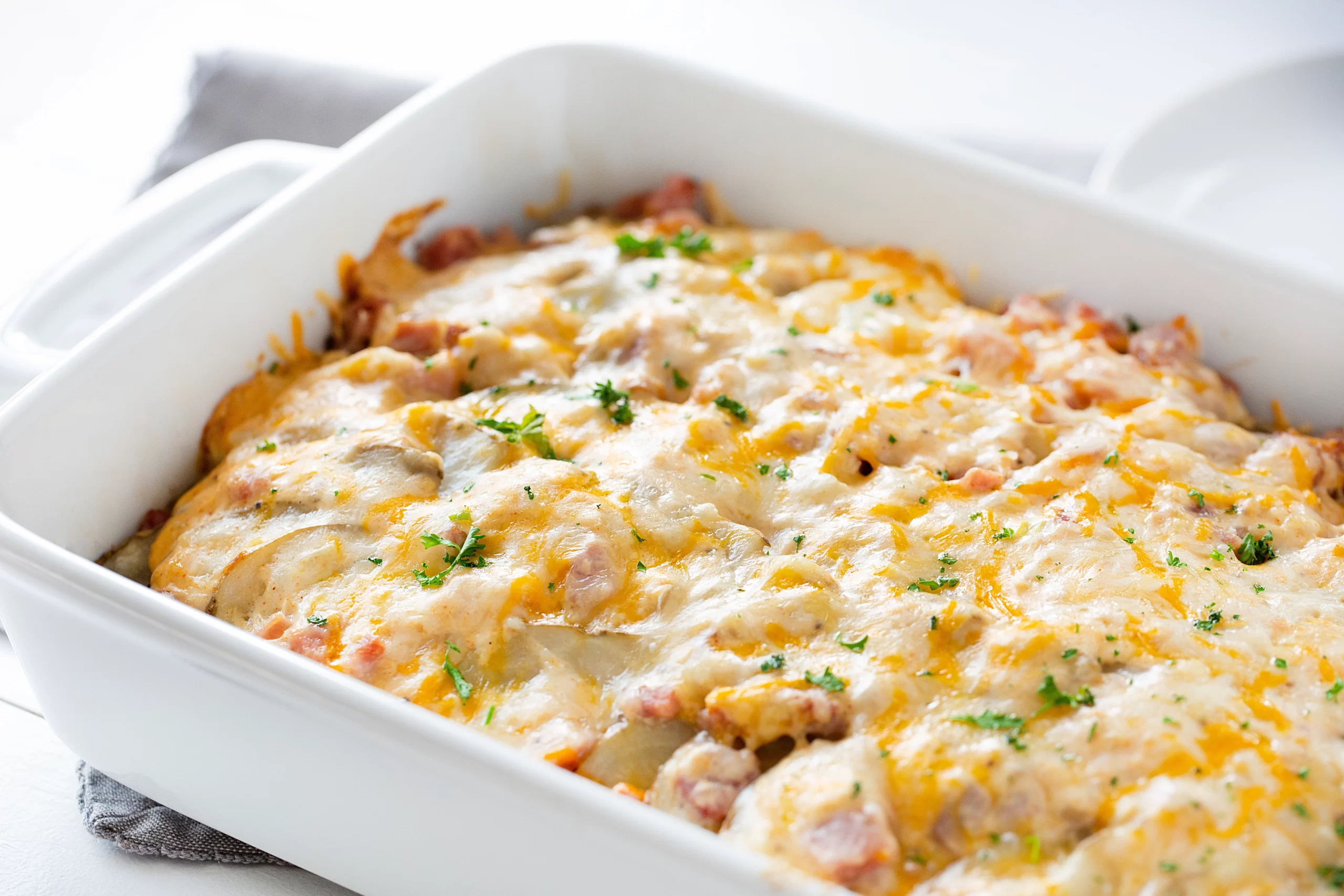 white baking dish with scalloped potatoes with ham and cheese