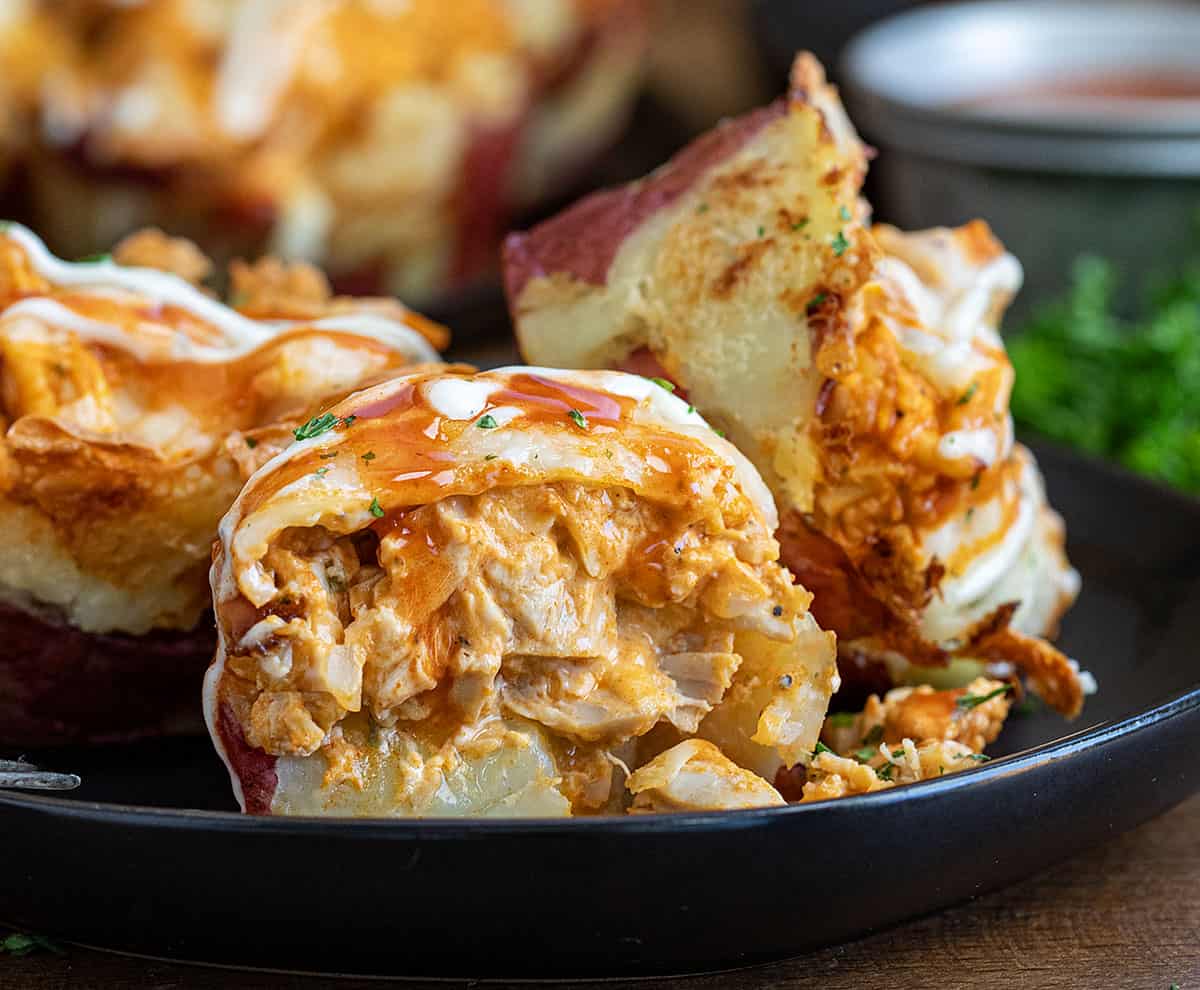 Sliced in half Buffalo Chicken Smashed Potato Cup on a black plate on a wooden table.