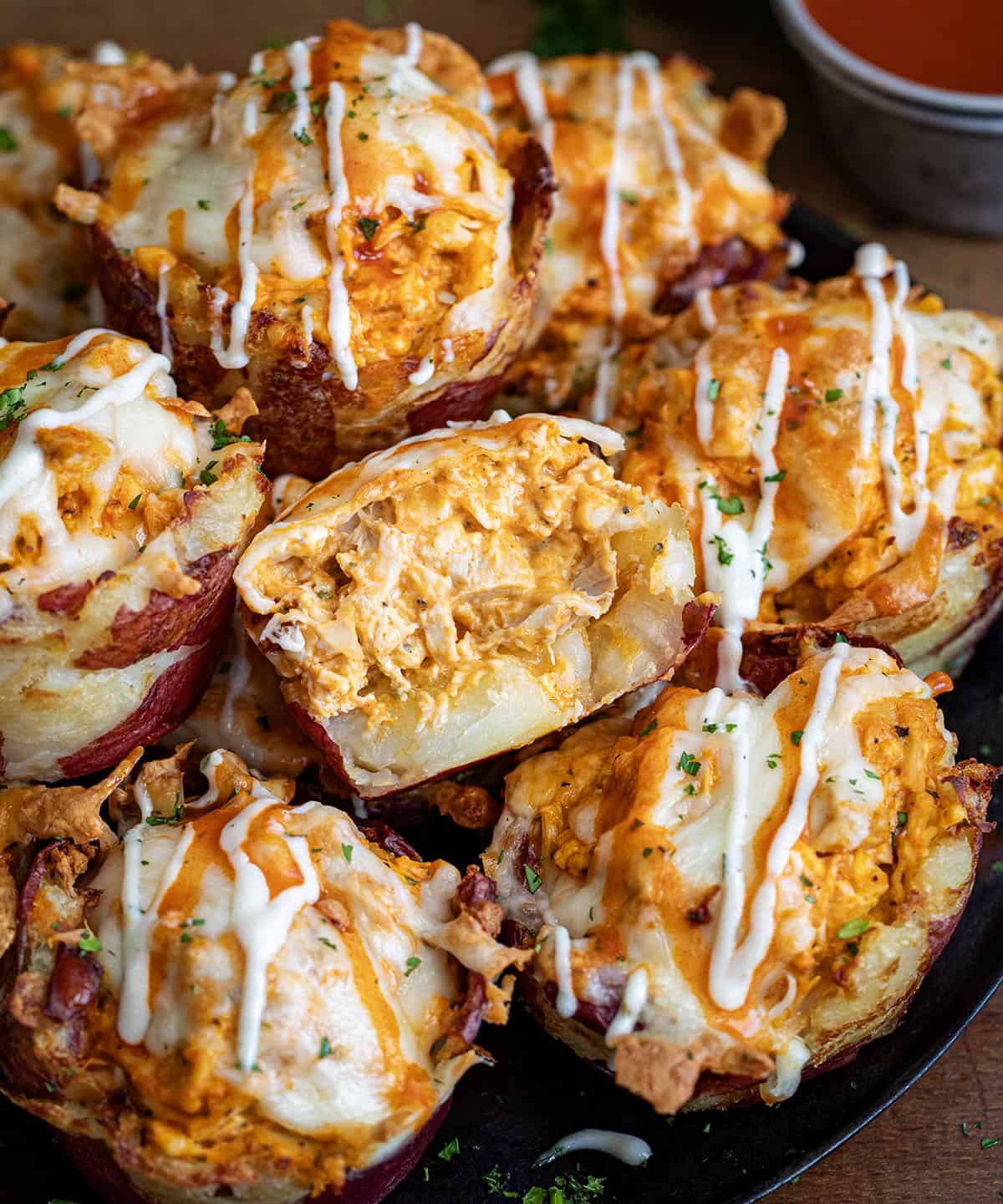 Many Buffalo Chicken Smashed Potato Cups on a platter with one cut in half showing buffalo chicken inside.