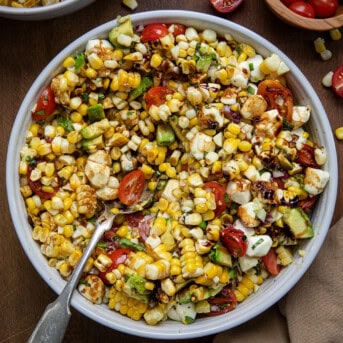 A big bowl of Caprese Corn Salad all mixed together with a spoon in it on a wooden table.