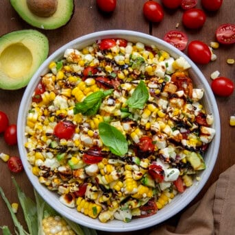 Bowl of Caprese Corn Salad with fresh tomatoes and avocado and corn on the cob from overhead.