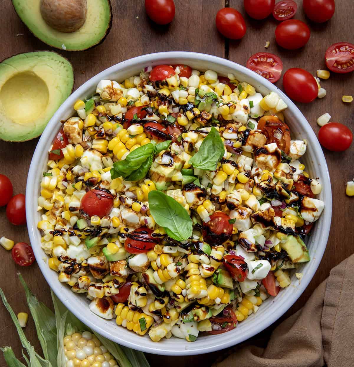 Bowl of Caprese Corn Salad with fresh tomatoes and avocado and corn on the cob from overhead. 