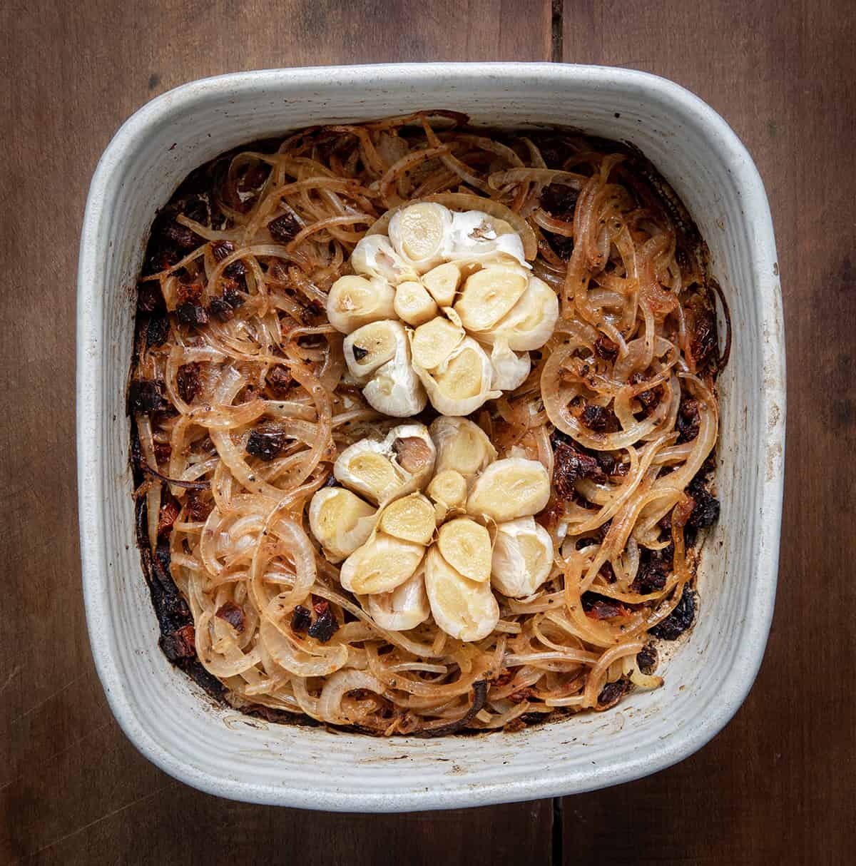 Roasted garlic and onions in a ceramic dish on a wooden table.