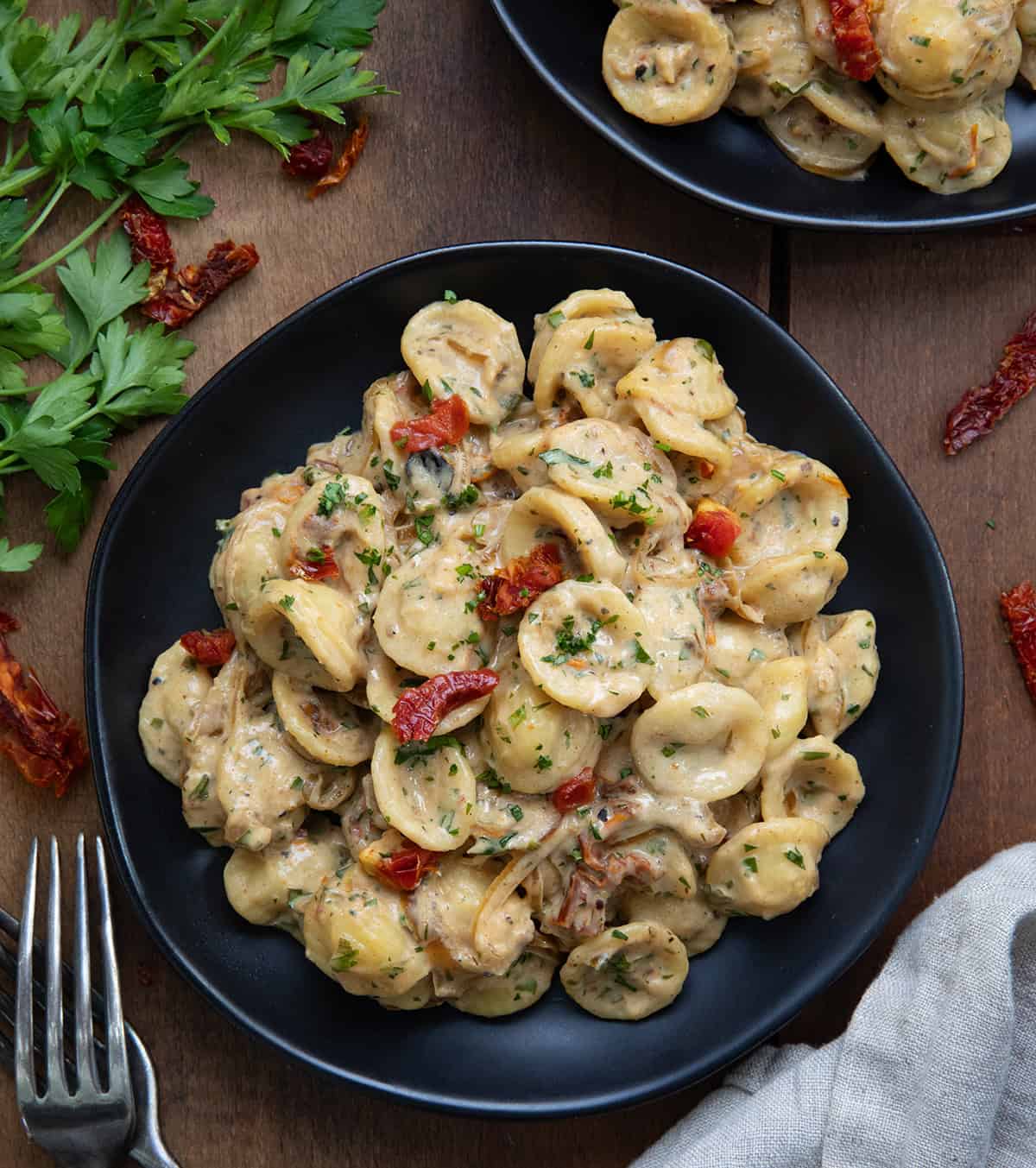 Black plates with Caramelized Onion Pasta on them with forks and sundried tomatoes around.