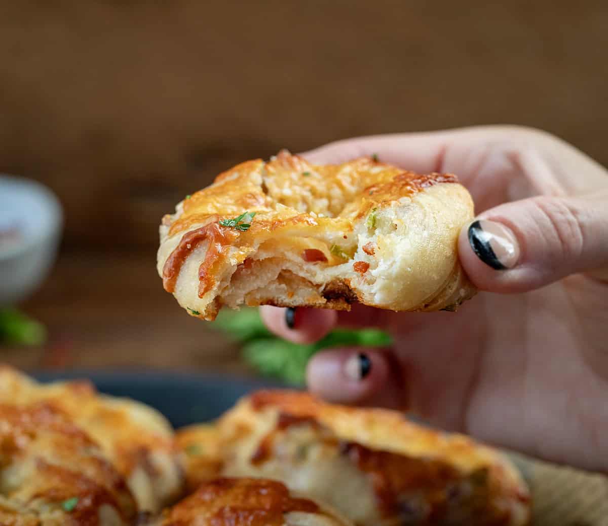 Hand holding a bit into Cheesy Bacon Jalapeno Twists With Garlic Butter.