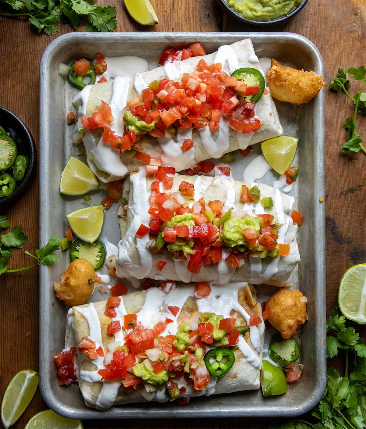 Three Cowboy Burrito's in a tray covered with pico and sour cream and a few cheese curds around.