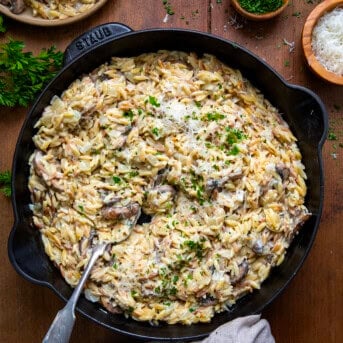 Skillet of Creamy Mushroom Orzo with a spoon in it on a wooden table from overhead.