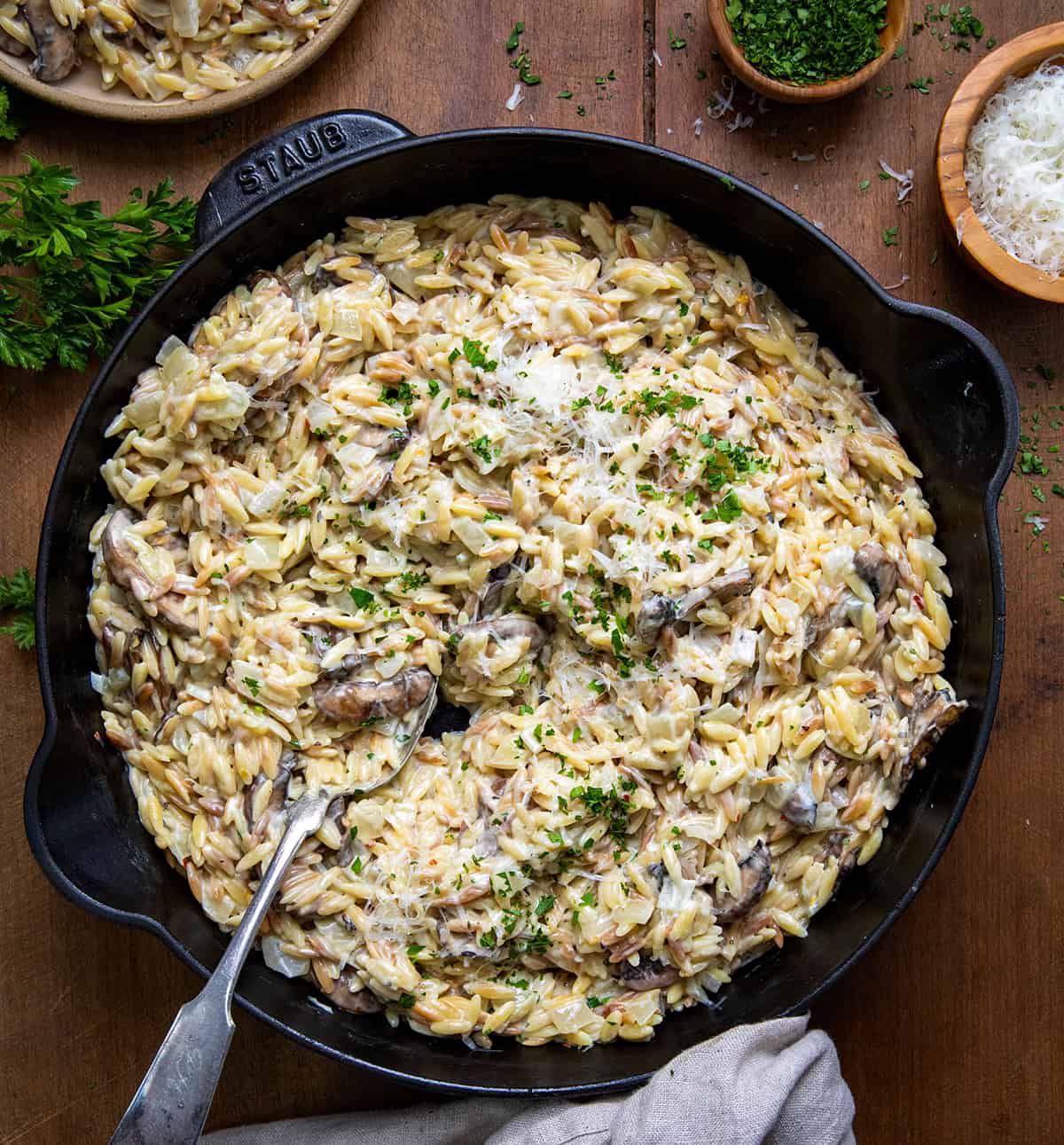 Skillet of Creamy Mushroom Orzo with a spoon in it on a wooden table from overhead.