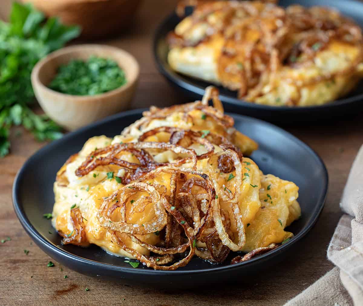 Black plates with Fried Onion Scalloped Potatoes on a wooden table.