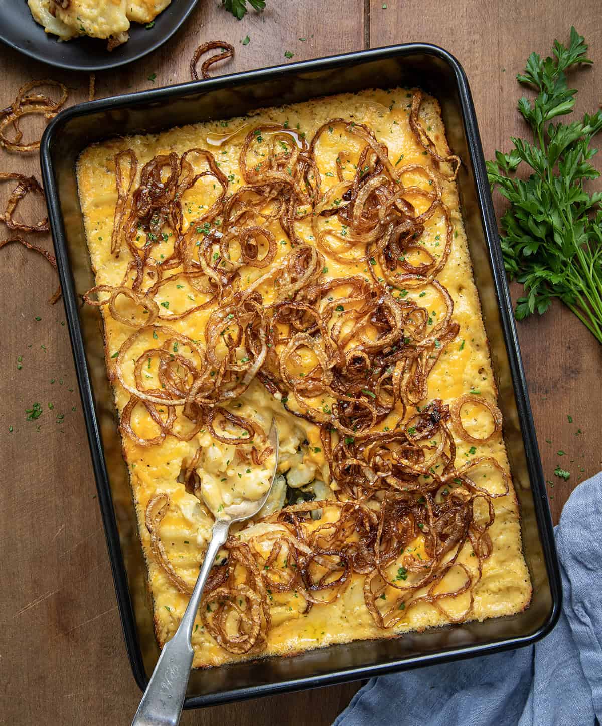 Casserole pan of Fried Onion Scalloped Potatoes with a spoon in it from overhead.