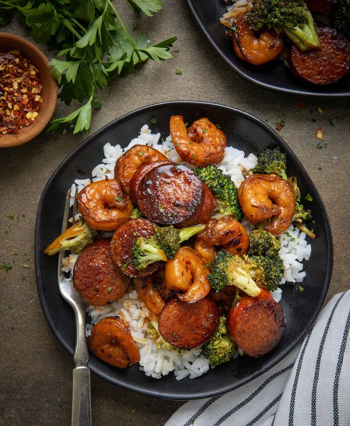 Black plates with Honey Garlic Shrimp, Sausage, and Broccoli on them with a form from overhead.