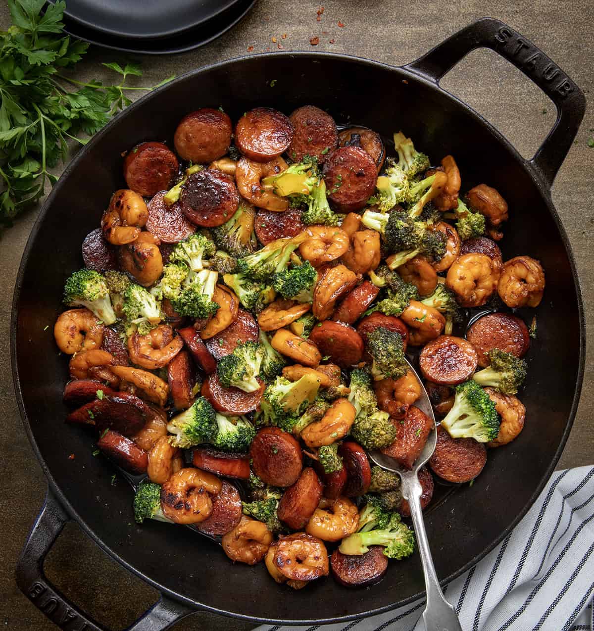 Skillet of Honey Garlic Shrimp, Sausage, and Broccoli with a spoon in it on a wooden table from overhead.