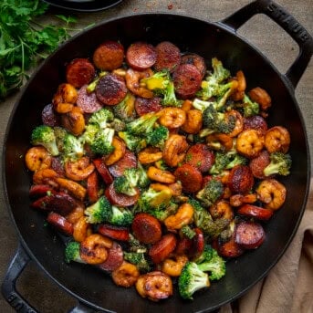 Skillet of Honey Garlic Shrimp, Sausage, and Broccoli on a wooden table from overhead.