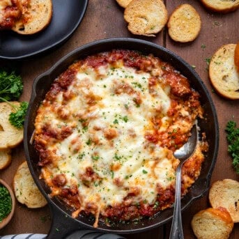 Skillet of Lasagna Dip with a spoon in it on a wooden table from overhead.