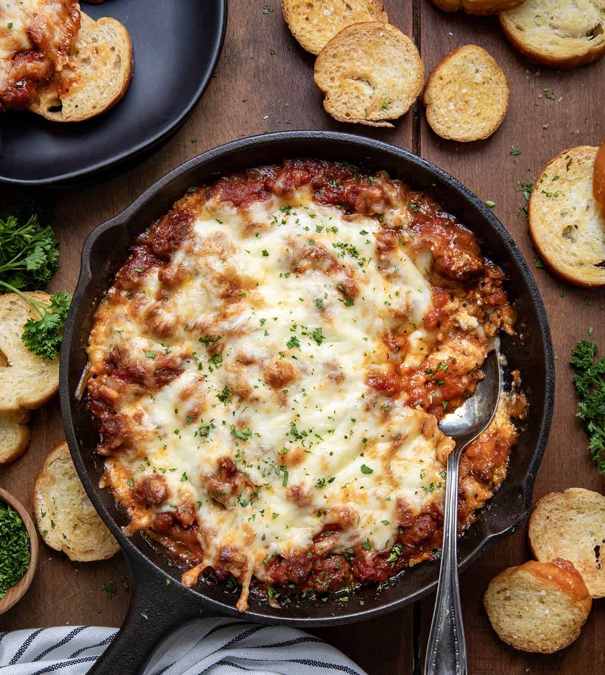 Skillet of Lasagna Dip with a spoon in it on a wooden table from overhead.