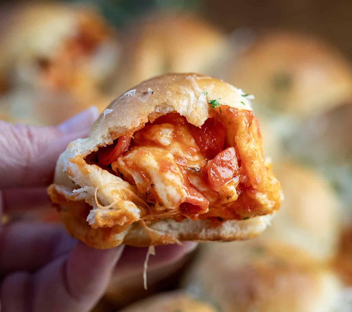 Hand holding a Pizza Bomb showing melted cheese and mini pepperoni inside.