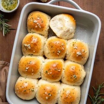 Pan of Rosemary Dinner Rolls on a wooden table with one roll removed and one on its side.